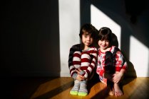 Junge und Mädchen im Schlafanzug sitzen im Sonnenlicht auf dem Fußboden — Stockfoto