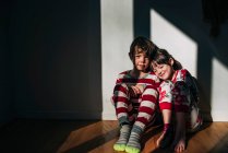 Menino e menina em seu pijama sentado no chão banhado pela luz do sol — Fotografia de Stock