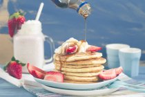 Pouring syrup onto a Stack of pancakes with fresh strawberries — Stock Photo