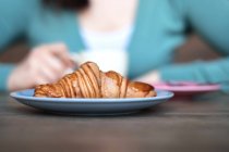 Croissant na frente de uma mulher bebendo café — Fotografia de Stock