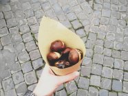 Woman hand holding roasted chestnuts wrapped in paper — Stock Photo