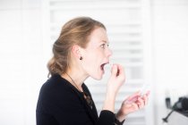 Woman standing in bathroom applying lip gloss — Stock Photo