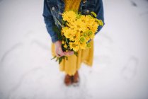 Chica de pie en la nieve sosteniendo un ramo de flores - foto de stock