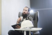 Человек, сидящий в кресле с цифровой табличкой с защитным шлемом на столе — стоковое фото