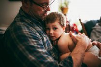 Father sitting on couch cuddling his son and kissing him on the head — Stock Photo