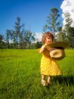 Fille debout dans un champ tenant un chapeau d'été, Brésil — Photo de stock