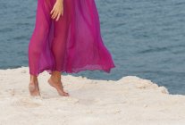 Recortado tiro de mujer en vestido rosa caminando en la playa - foto de stock