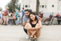 Coppia sorridente seduta su uno skateboard in una piazza della città — Foto stock