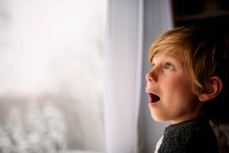 Überraschter Junge schaut im Winter aus dem Fenster — Stockfoto