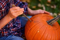 Boy carving a Halloween pumpkin in the garden, United States — Stock Photo