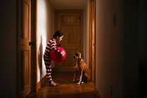 Girl standing in the hallway holding a giant ball playing with her dog — Stock Photo
