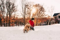 Мальчик играет в снегу со своей золотой собакой-ретривером — стоковое фото