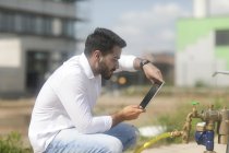 Homem sentado ao ar livre tirando uma foto de um hidrante usando um tablet digital — Fotografia de Stock