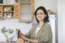 Mujer sonriente vertiendo granos de café frescos en un molinillo de café - foto de stock
