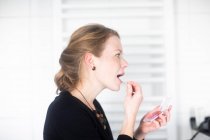 Frau steht im Badezimmer und trägt Lipgloss auf — Stockfoto