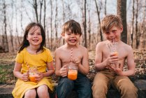 Tres niños sentados en una pared disfrutando de una bebida de verano - foto de stock