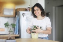 Femme souriante s'occupant d'une plante en pot dans sa cuisine — Photo de stock