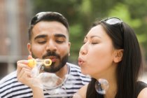 Couple tenant une baguette à bulles soufflant des bulles de savon — Photo de stock