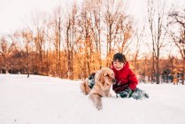 Junge sitzt mit seinem Golden Retriever-Hund im Schnee — Stockfoto