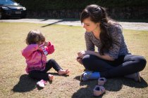 Menina sentada no parque brincando com uma meia com a mãe, Brasil — Fotografia de Stock