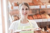 Asistente de ventas sonriente en una panadería con una bandeja de muestras - foto de stock