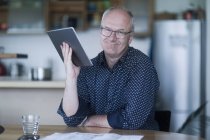 Porträt eines lächelnden Mannes, der am Tisch sitzt und ein digitales Tablet hält — Stockfoto