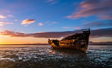 Розбитий човен на заході сонця над морем — стокове фото