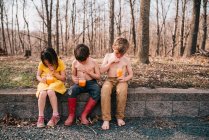 Tre bambini seduti su un muro a gustarsi un drink estivo — Foto stock
