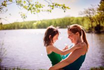 Mother standing by a lake carrying her daughter — Stock Photo