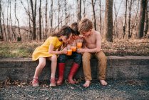Drei Kinder sitzen auf einer Mauer und genießen Sommergetränke — Stockfoto