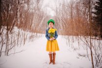 Sonriente chica de pie en la nieve sosteniendo un ramo de flores - foto de stock