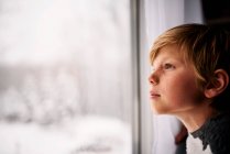 Junge schaut im Winter aus dem Fenster — Stockfoto