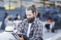 Uomo sorridente seduto all'aperto utilizzando un tablet digitale — Foto stock