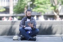 Чоловік сидить на скейтборді за допомогою цифрового планшета — стокове фото