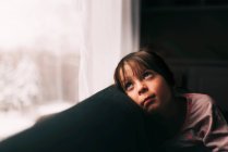 Ragazza seduta su un divano guardando attraverso una finestra — Foto stock