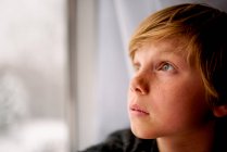 Мальчик зимой смотрит в окно — стоковое фото