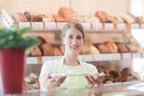Улыбающийся помощник по продажам в пекарне с подносом образцов — стоковое фото