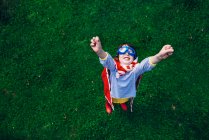 Menina vestindo um traje de super-herói em pé no jardim com os braços no ar — Fotografia de Stock