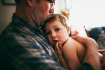 Vater sitzt auf Couch und kuschelt seinen Sohn und küsst ihn auf den Kopf — Stockfoto