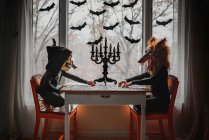 Dos niños con disfraces de Halloween sentados junto a una ventana haciendo un rompecabezas, Estados Unidos - foto de stock