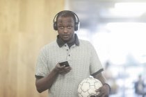Человек в наушниках с мобильным телефоном и футбольным мячом — стоковое фото