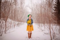 Smiling girl standing in the snow holding a bunch of yellow flowers — Stock Photo