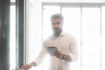 Чоловік стоїть в офісі за допомогою цифрового планшета — стокове фото