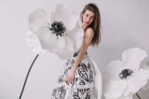 Женщина в бумажном платье, стоящая рядом с искусственными цветками анемона — стоковое фото