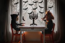 Two children in Halloween costumes sitting by a window doing a jigsaw puzzle, United States — Stock Photo