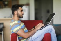 Man sitting in an armchair working on his laptop computer — Stock Photo