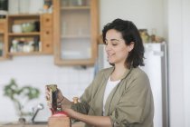 Жінка вливає свіжі кавові зерна в кавомолку — стокове фото