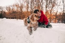 Niño abrazando a su perro recuperador de oro en la nieve - foto de stock