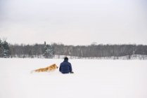 Человек сидит в снегу со своей золотой собакой-ретривером — стоковое фото