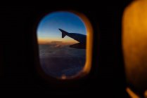 View of an airplane wing through the window at sunset — Stock Photo